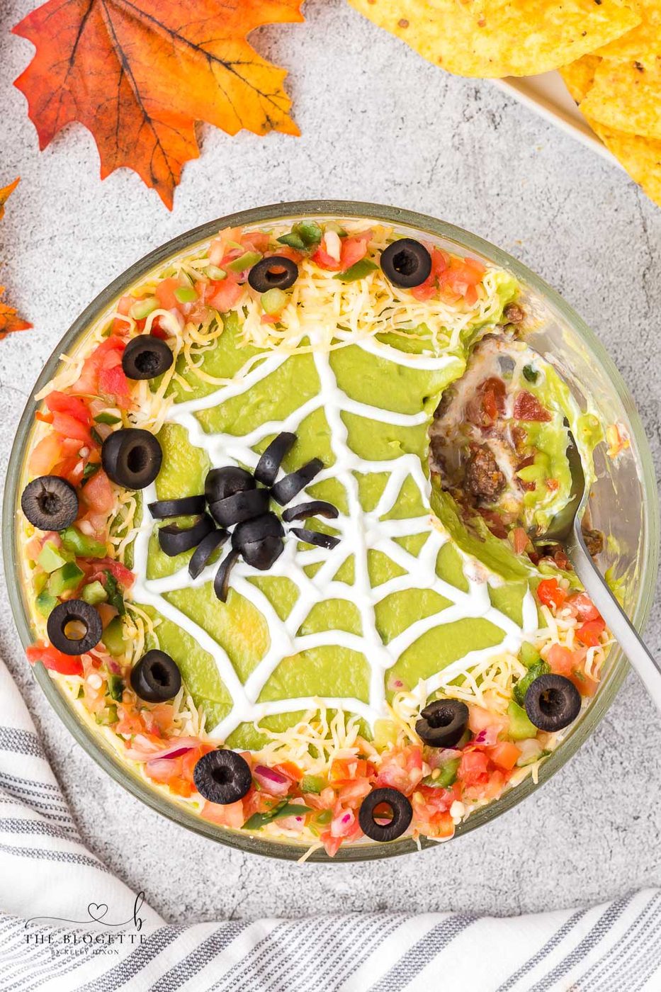 Spider Web 7 Layer Dip is just what your Halloween needs! A spooky little olive spider sits atop a sour cream spider web on layers of meat, beans, cheese, guacamole, and more!