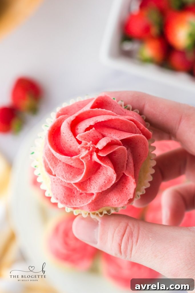 A freshly frosted Strawberry Lemon Cupcake being piped with strawberry frosting.