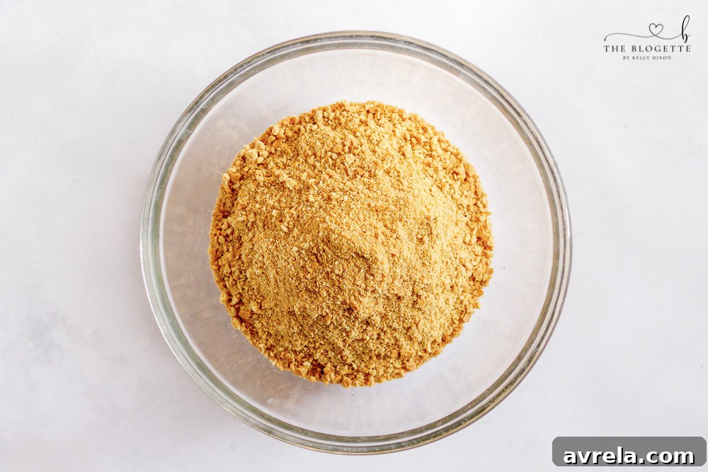 Graham cracker crust being pressed into a pan lined with parchment paper.