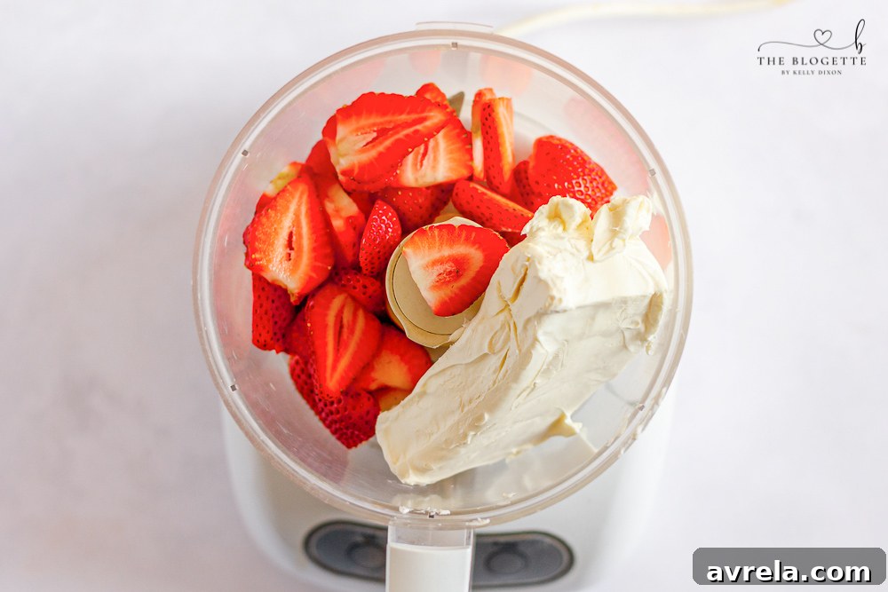 Cream cheese, strawberries, sugar, and vanilla extract being blended in a food processor.