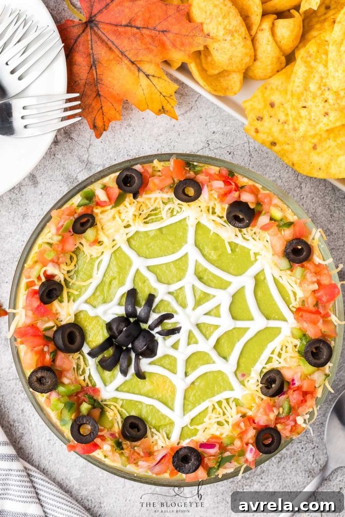 A festive Spider Web 7 Layer Dip featuring a spooky olive spider on a sour cream web, perfect for Halloween parties.