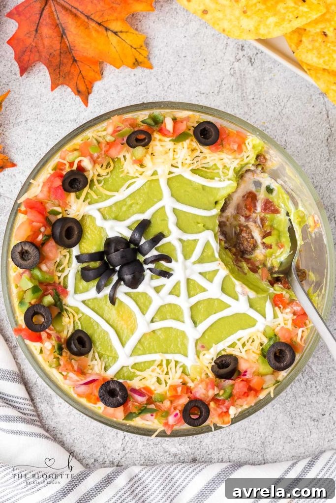 A vibrant Spider Web 7 Layer Dip with a variety of colorful layers and an olive spider, ready for Halloween.