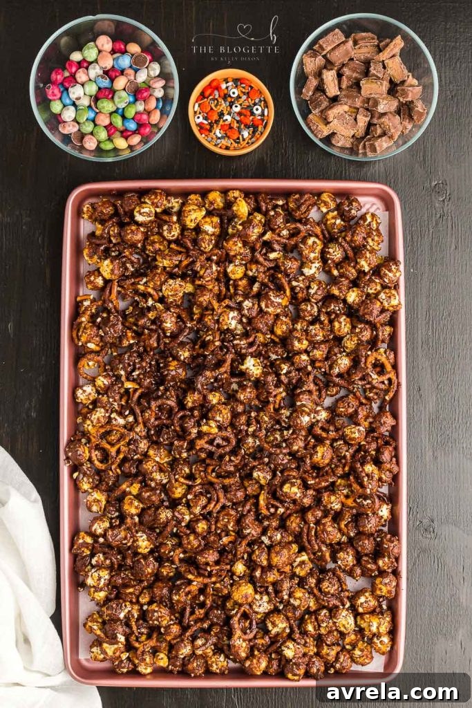 Fright Night Fuel 7 A finished Halloween Snack Mix, spread evenly on parchment paper, adorned with colorful candies and sprinkles, ready to be chilled.