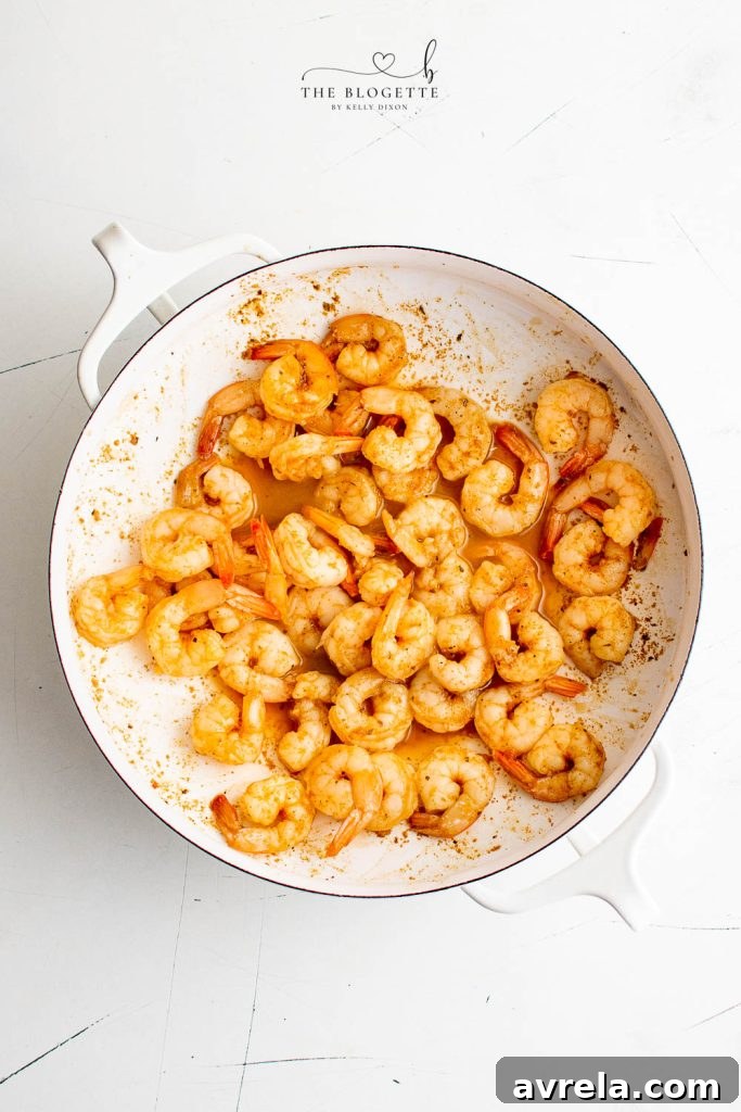 Lemon Garlic Butter Scampi Pasta 5 Shrimp cooking in a skillet with Cajun seasoning, turning pink and curling.