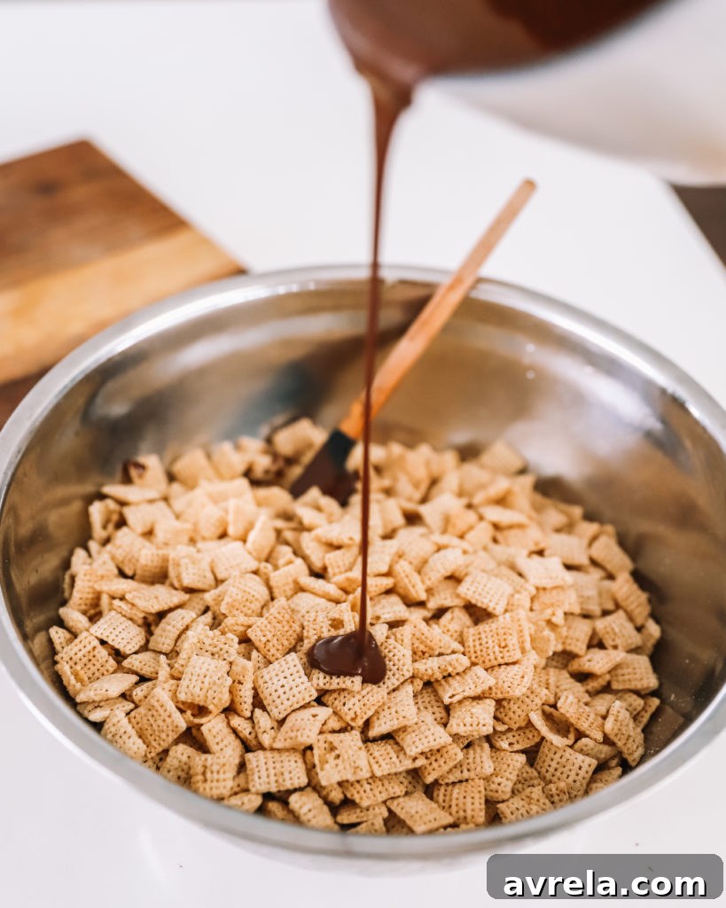 A hand reaching into a bowl of Muddy Buddies, showcasing the texture and powdered sugar coating.