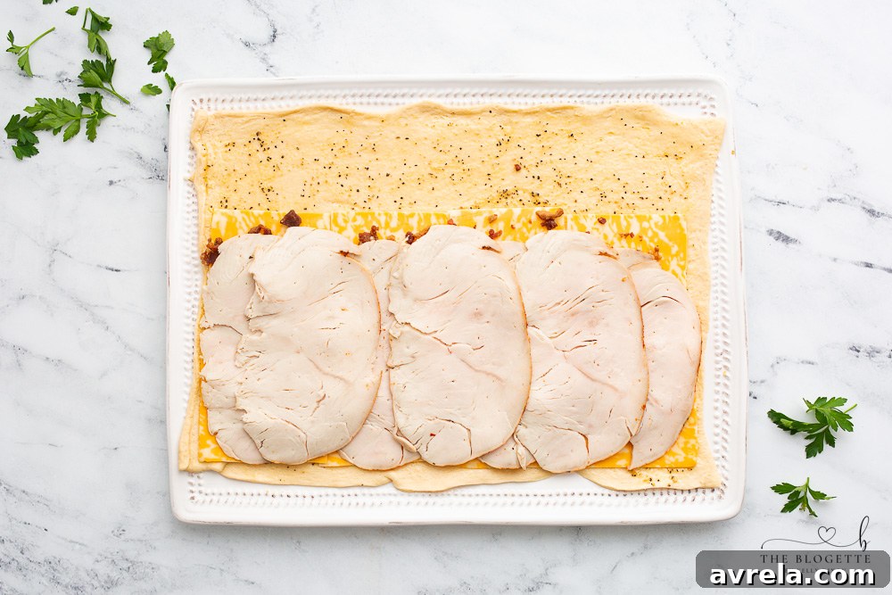 Turkey slices covering bacon and cheese on crescent dough.