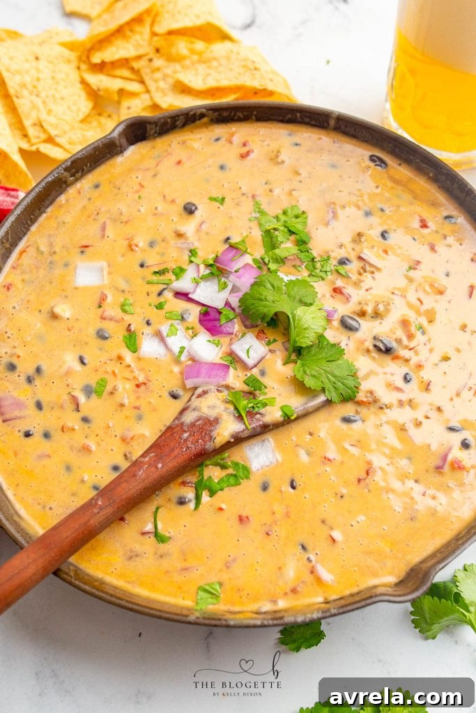 A close-up of creamy Loaded Queso Dip with visible chunks of beef, beans, and vibrant spices.
