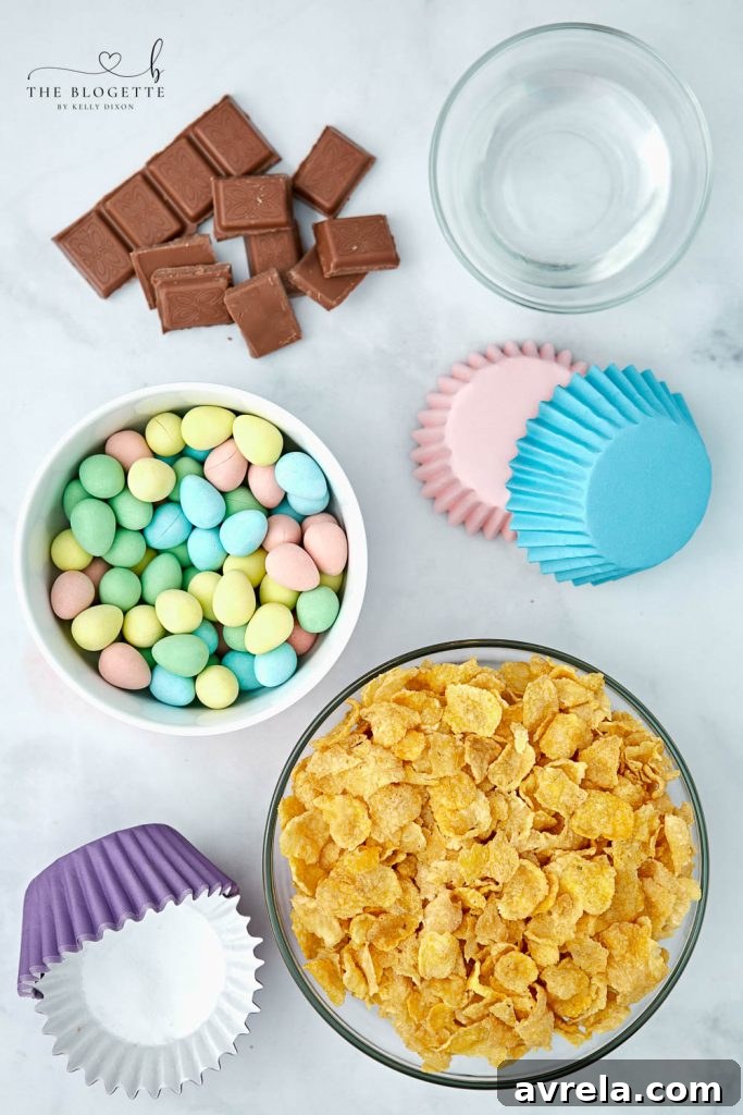 Chocolate bird nest ingredients laid out on a table: cornflakes, chocolate bars, coconut oil, and a selection of mini candy eggs.