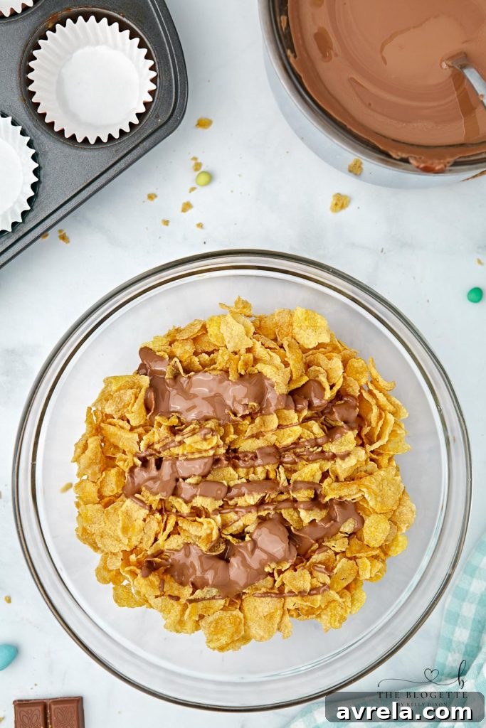 Close-up of cornflakes being gently mixed with melted chocolate in a bowl, showing thorough coating for the nests.