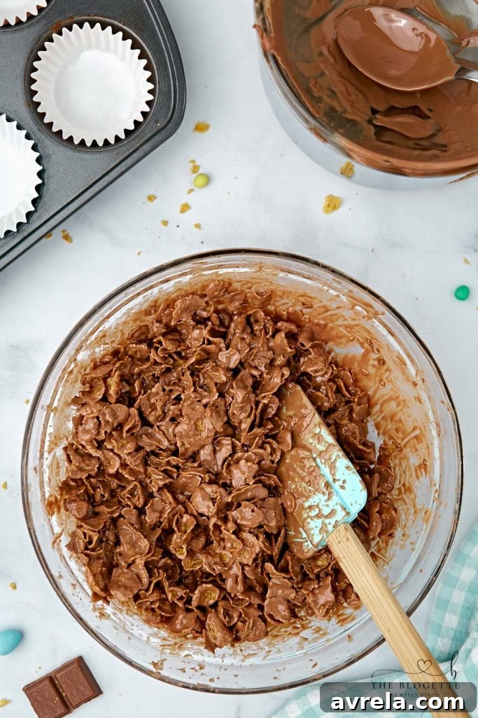 Chocolate covered cornflakes carefully spooned into individual cupcake liners within a muffin pan, forming nest shapes.