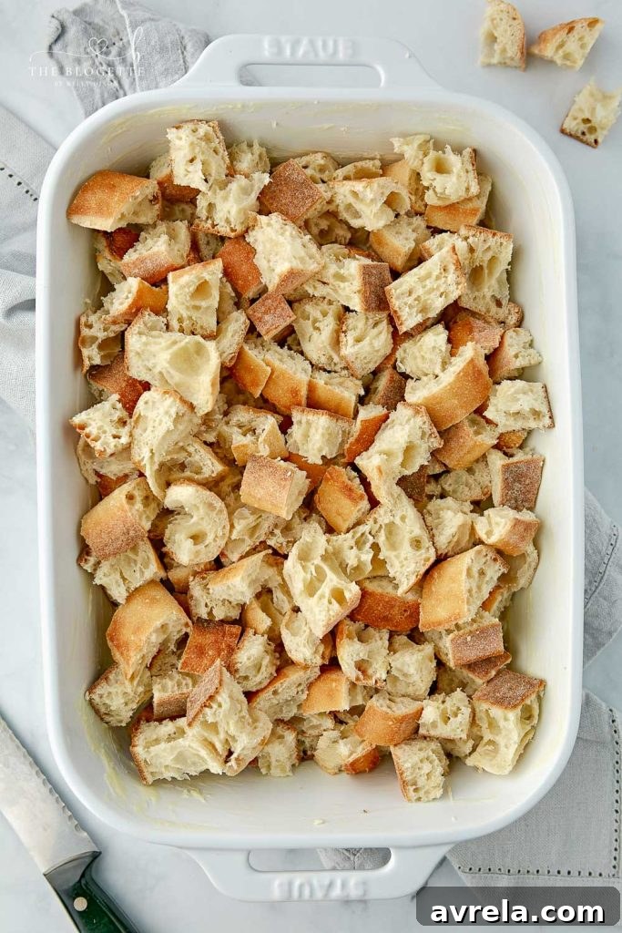 Morning Glory French Toast Bake 5 Hands cutting French bread into uniform cubes, preparing it for the casserole.
