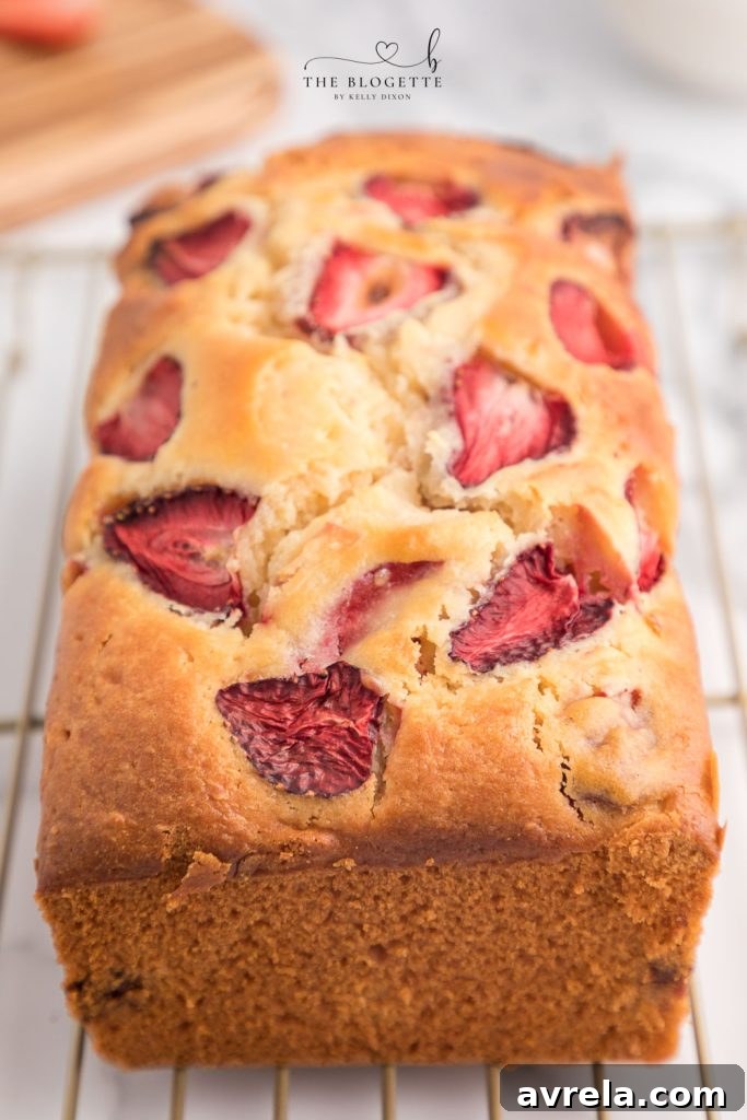 A whole Strawberry Bread loaf with sliced strawberries on top, cooling on a wire rack.