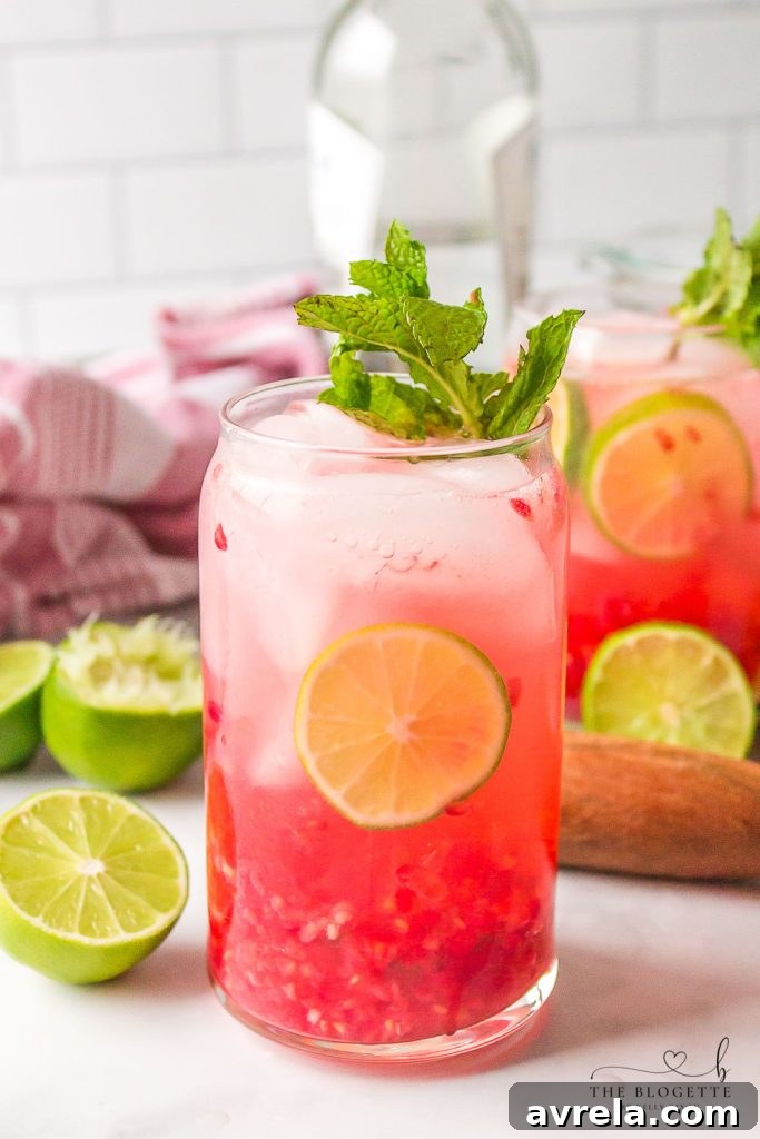 A vibrant Raspberry Mojito in a tall glass, garnished with fresh raspberries, lime wedges, and mint sprigs, set against a summer backdrop.