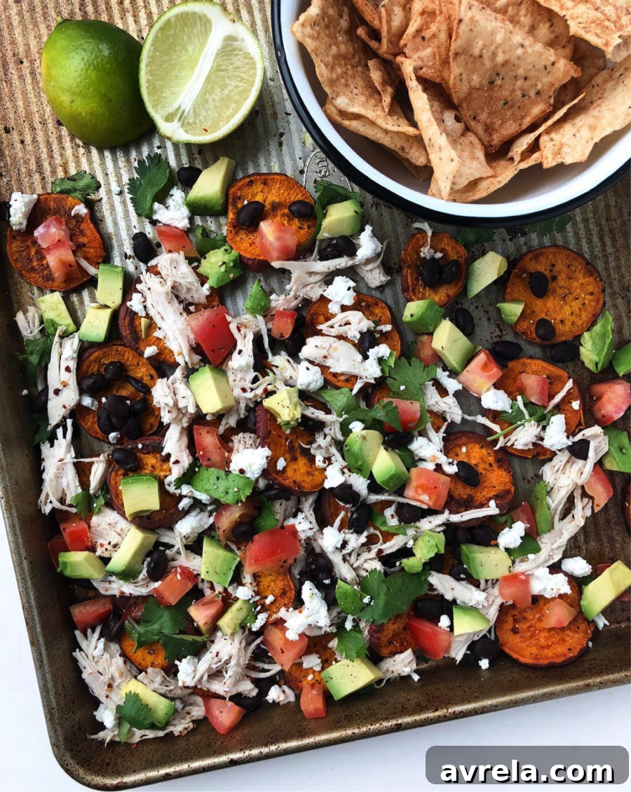 Delicious Sweet Potato Nachos piled high with shredded chicken, black beans, avocado, and fresh cilantro, served on a rustic baking sheet.