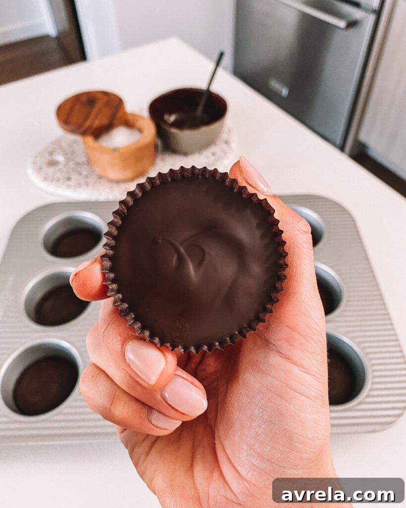 Two perfect homemade Reese's Peanut Butter Cups, one unwrapped revealing the creamy peanut butter, next to another still in its signature brown fluted wrapper.