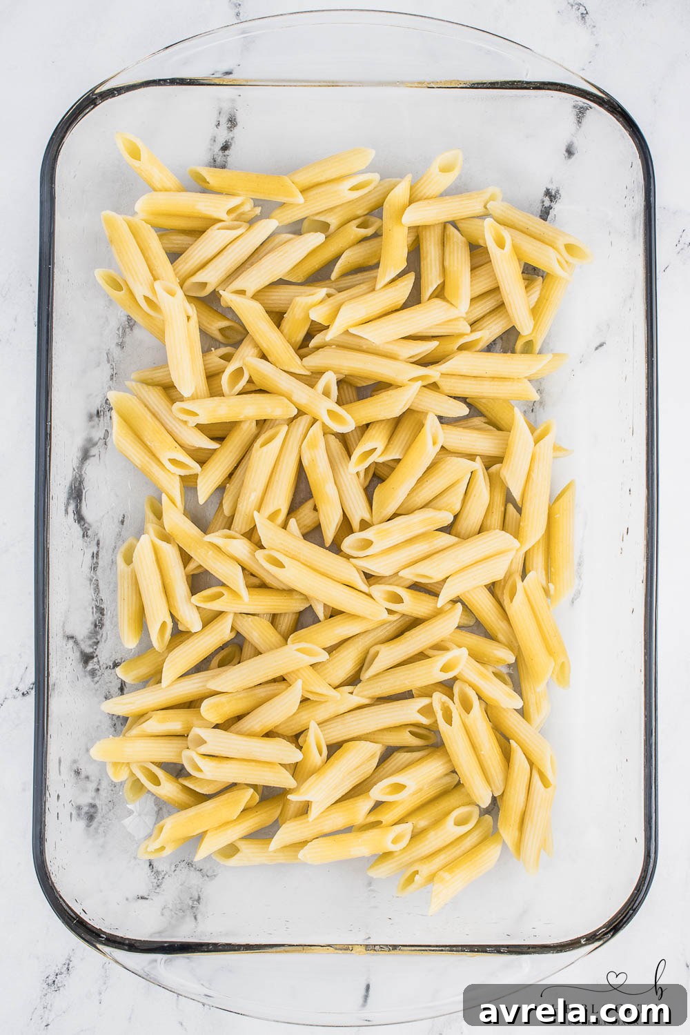 Cooked penne pasta in a baking dish, ready for the next layer of the pizza casserole.