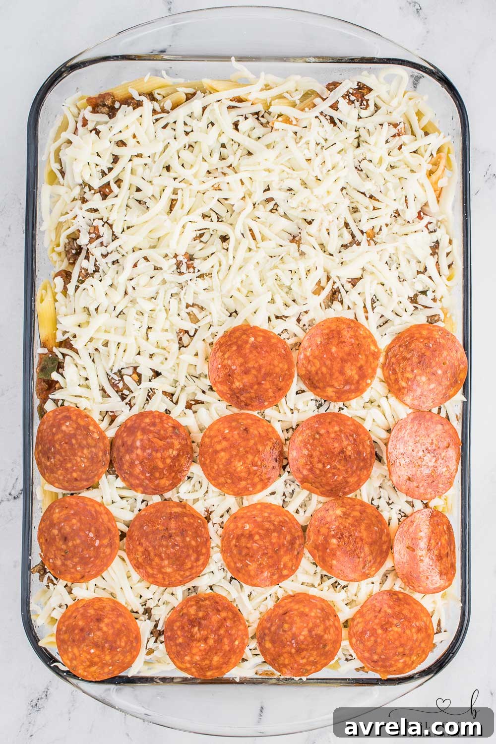 A final layer of pepperoni slices generously placed over melted cheese on a pizza casserole.