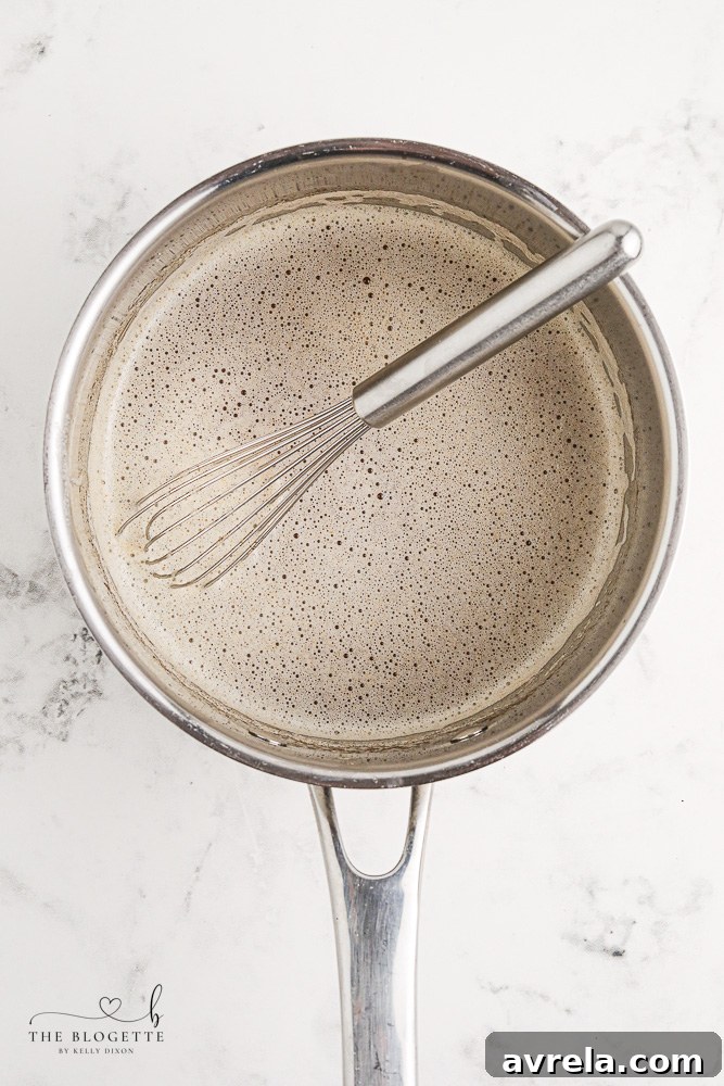 Unflavored gelatin being whisked into hot apple cider in a saucepan.