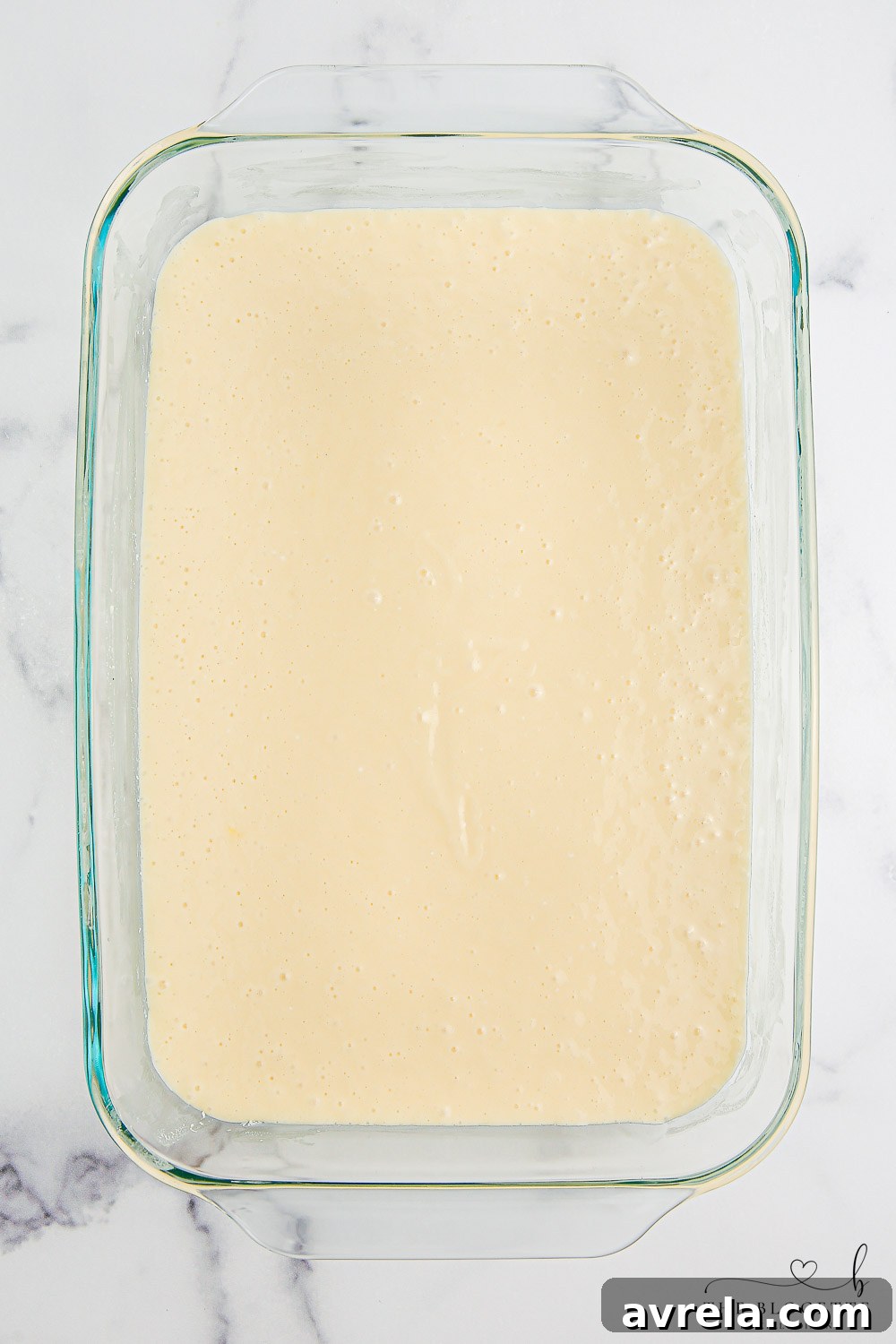 Golden yellow cake batter freshly mixed and smoothly poured into a 9x13 inch baking dish, perfectly ready for the oven, marking a crucial first step for the Boston Cream Poke Cake.