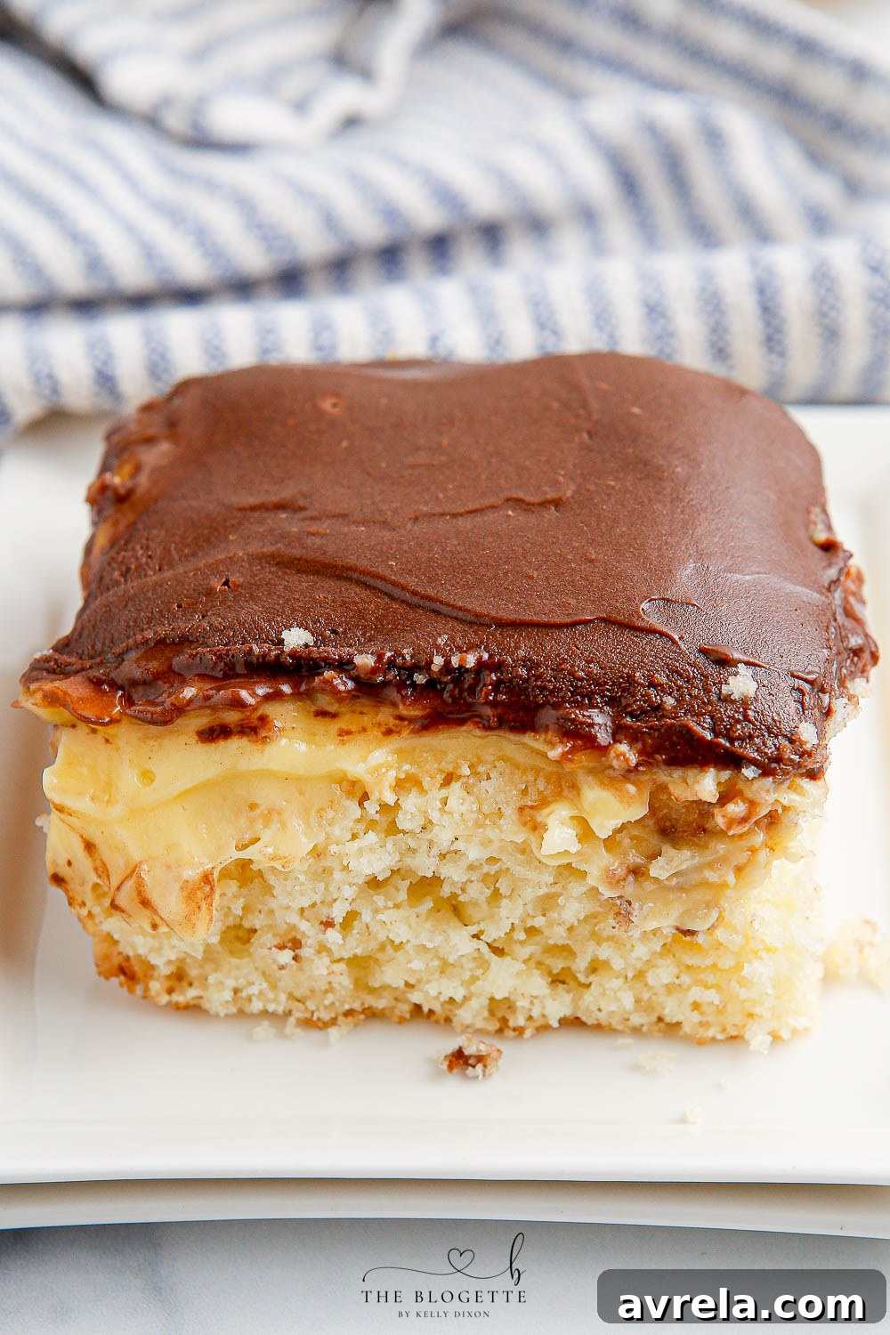 A close-up shot of a perfectly prepared Boston Cream Poke Cake, showcasing its beautiful layers of moist cake, rich vanilla pudding, and shiny chocolate top, confirming its appealing texture and ease of preparation.