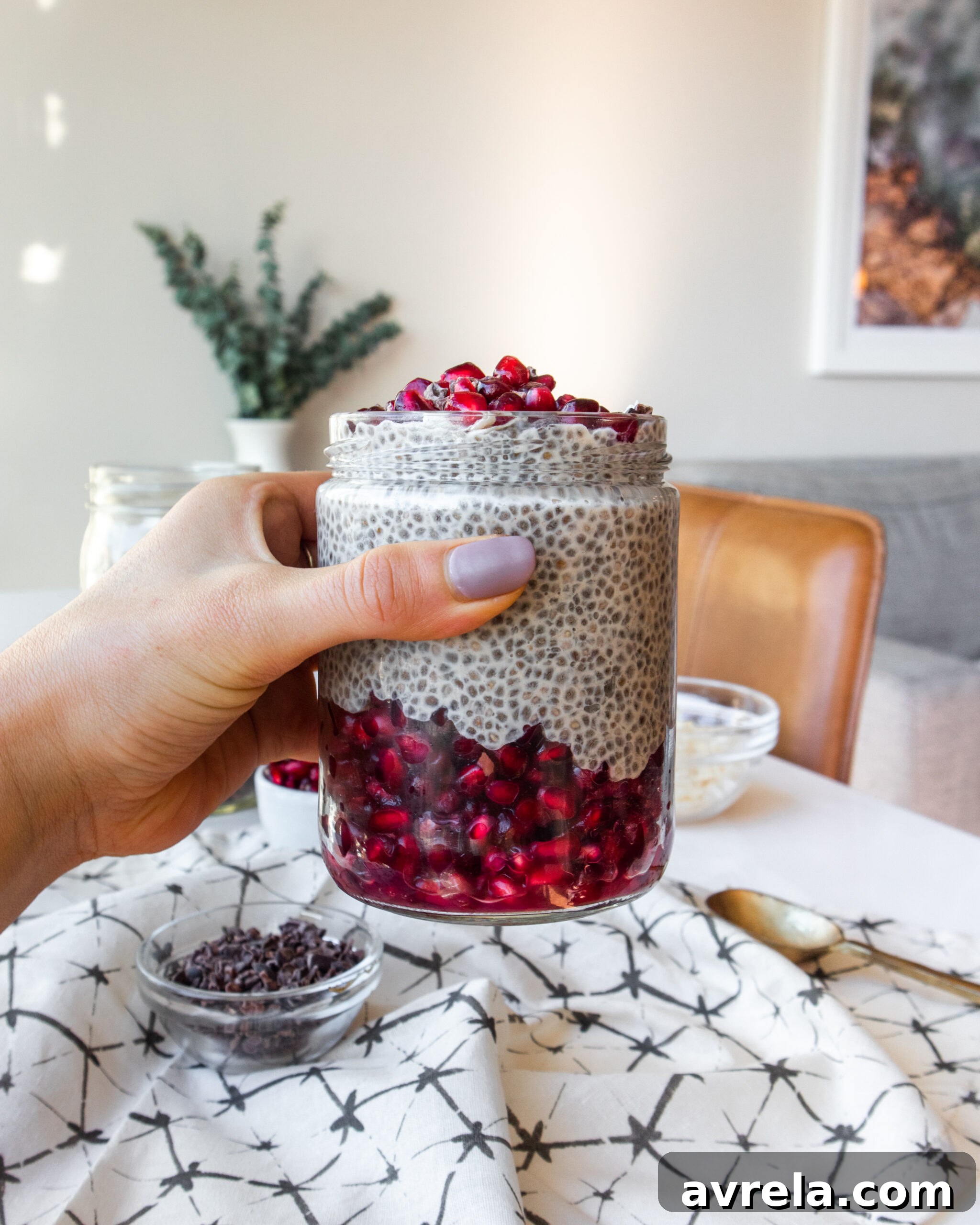 A beautifully layered creamy coconut chia pudding with vibrant pomegranate arils, cacao nibs, and shredded coconut in a glass jar, perfect for a healthy breakfast or snack.