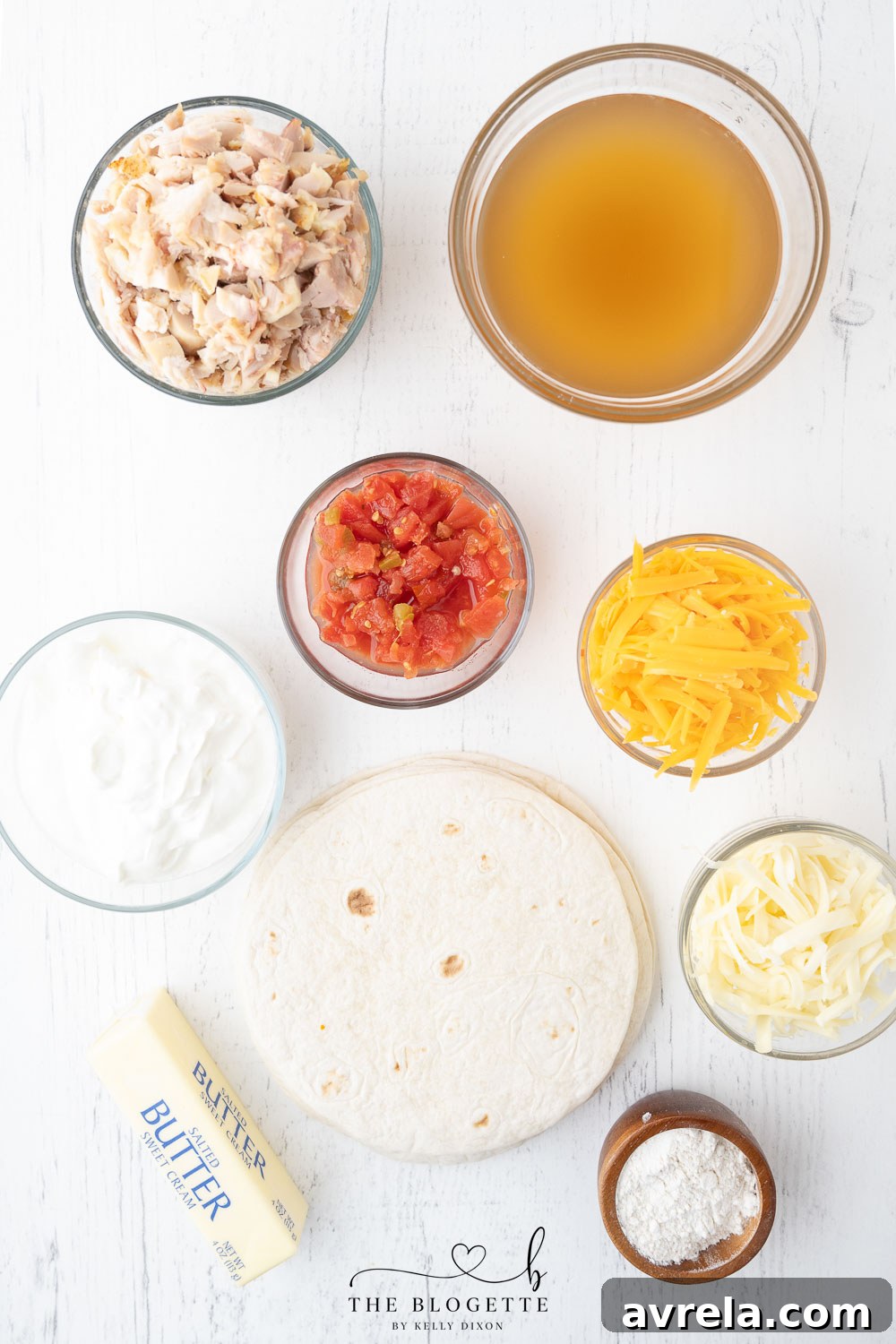 Assortment of fresh ingredients laid out on a kitchen counter: shredded chicken, cheeses, Rotel, sour cream, and tortillas.