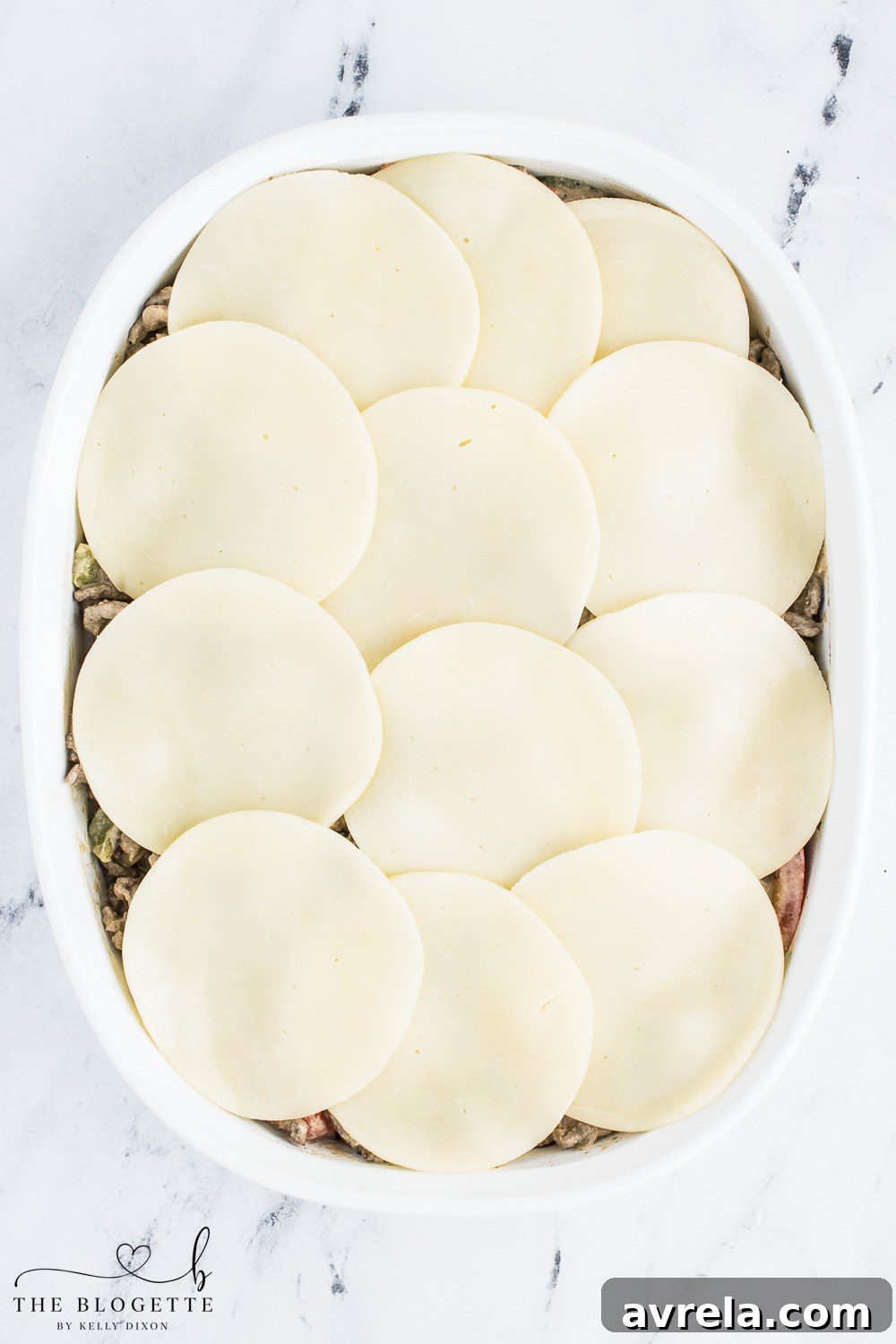 Philly Cheesesteak Comfort Bake 9 Slices of provolone cheese neatly arranged on top of the cheesesteak mixture in a casserole dish, ready for baking until golden and bubbly.