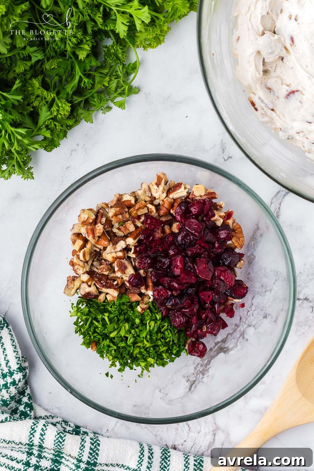 A bowl filled with a colorful mixture of chopped pecans, dried cranberries, and fresh parsley, ready to coat the goat cheese truffles.