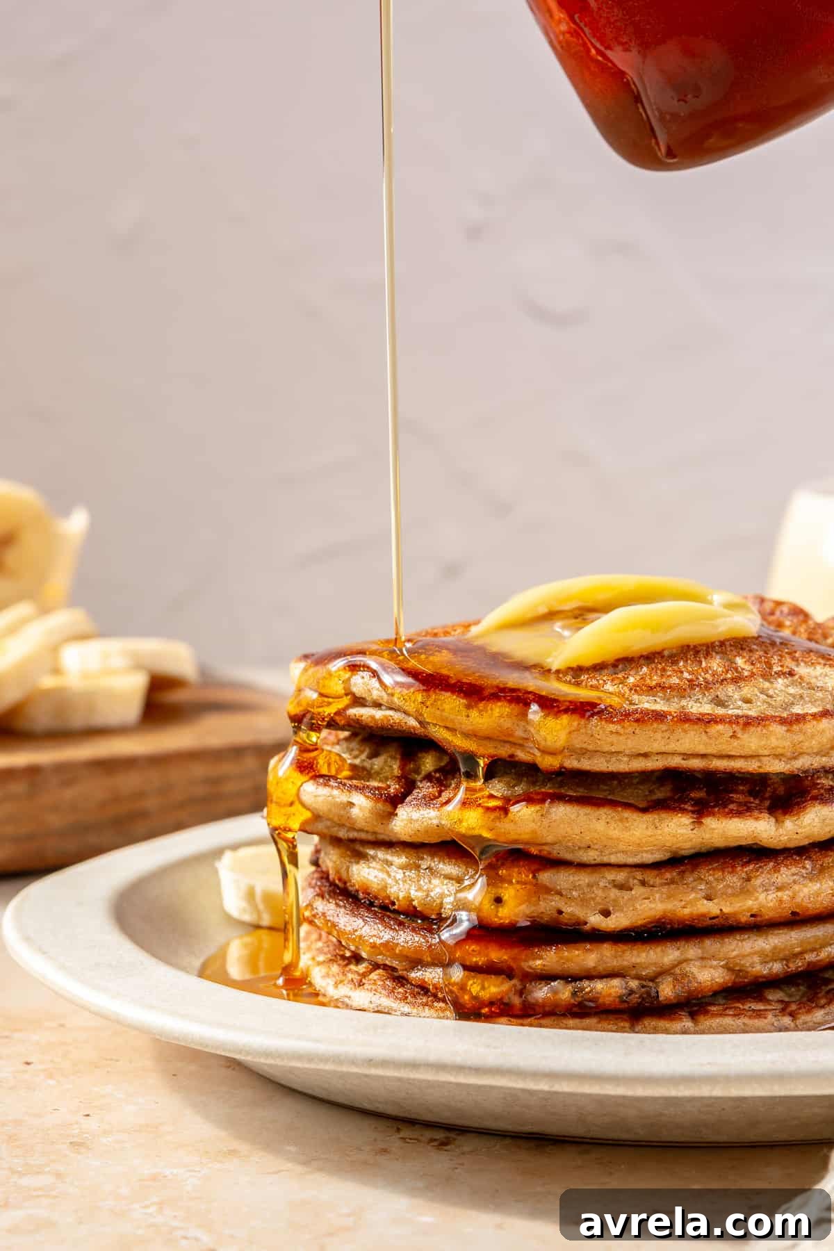 A stack of High-Protein Blender Banana Oat Pancakes topped with sliced bananas and maple syrup.