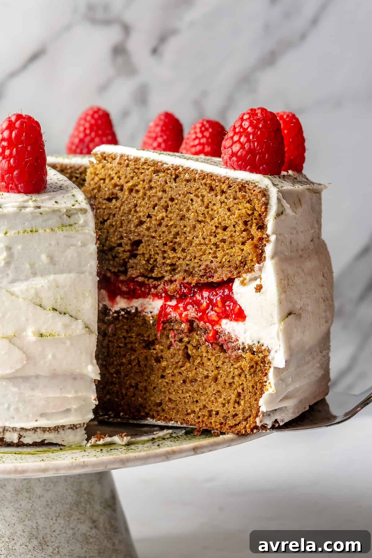 A beautifully sliced gluten-free matcha lemon vanilla cake, revealing its moist layers and raspberry filling.