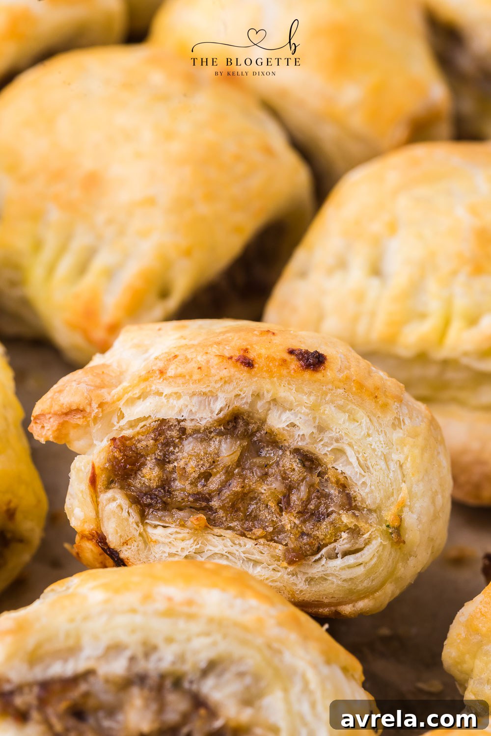 A large platter filled with freshly baked, golden brown sausage rolls, garnished with fresh herbs.