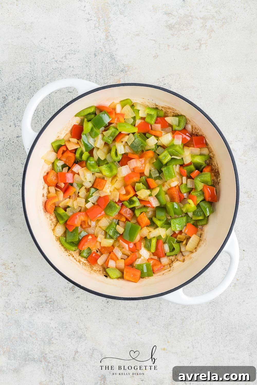 Close-up of sautéed onions and peppers in a large skillet, softened and vibrant.