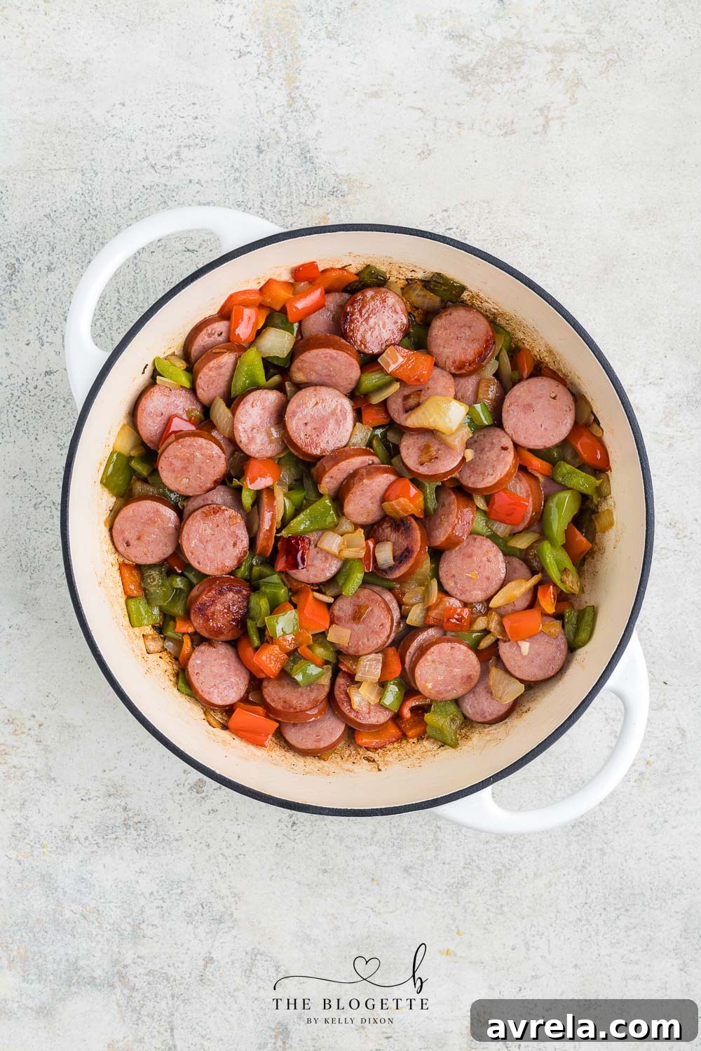 Smoked sausage slices added to sautéed onions and peppers in a skillet.