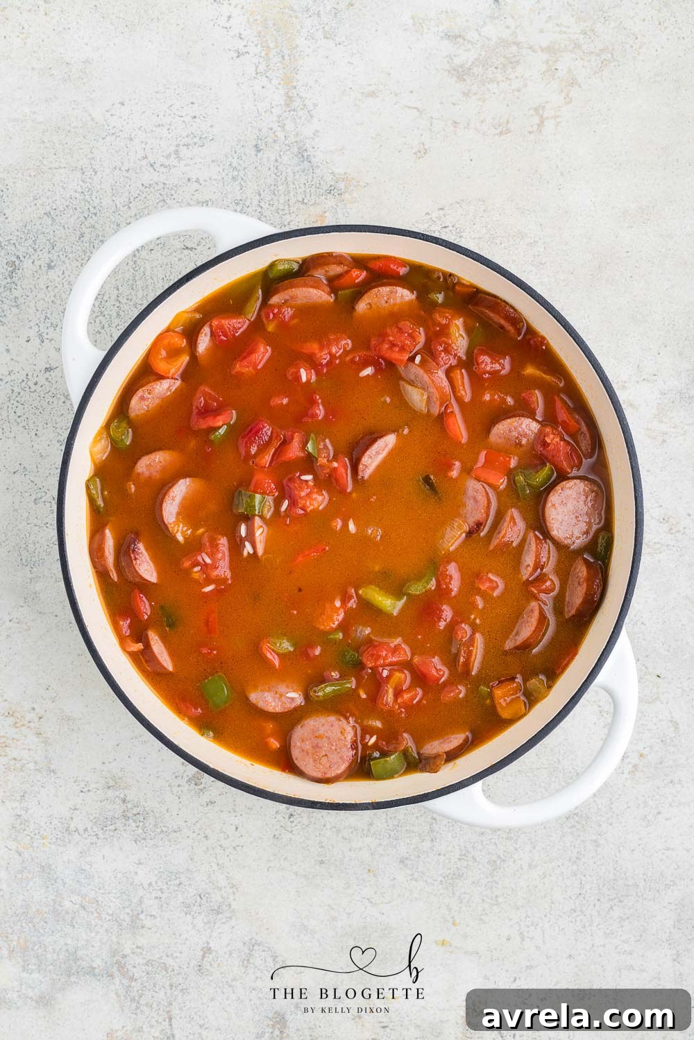 Sausage, rice, and vegetables simmering in a vibrant tomato sauce in a skillet.