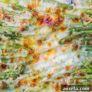 A square image of cheesy garlic baked green beans, perfectly golden and bubbly, with a focus on the melted cheese.