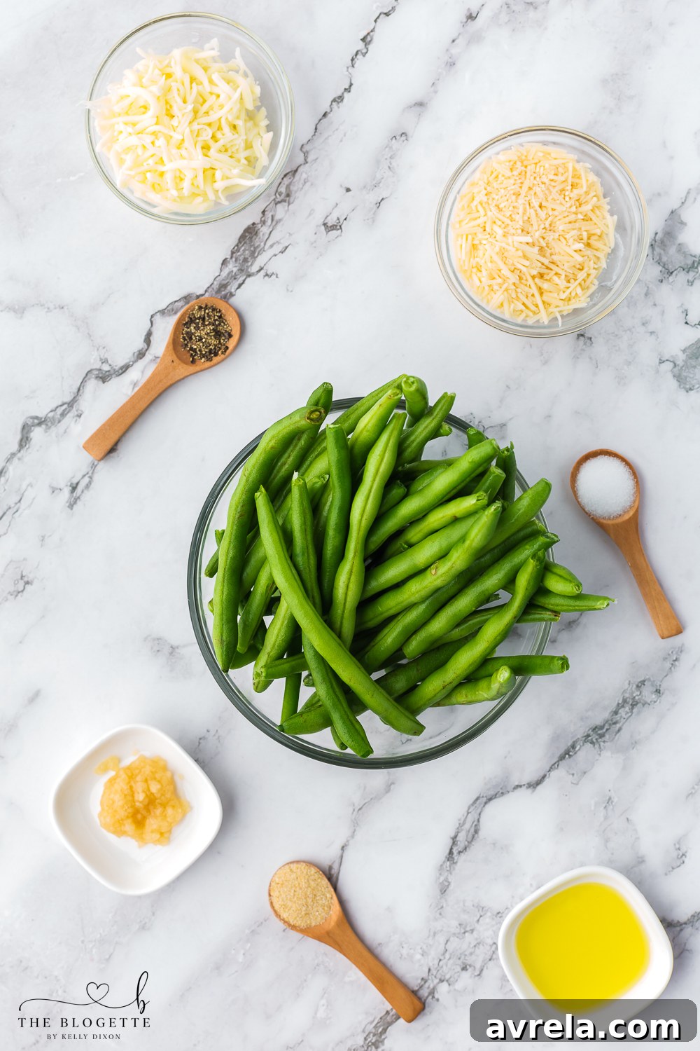 A collection of fresh ingredients laid out, including green beans, olive oil, onion powder, minced garlic, salt, pepper, parmesan, and mozzarella cheese, ready for preparation.