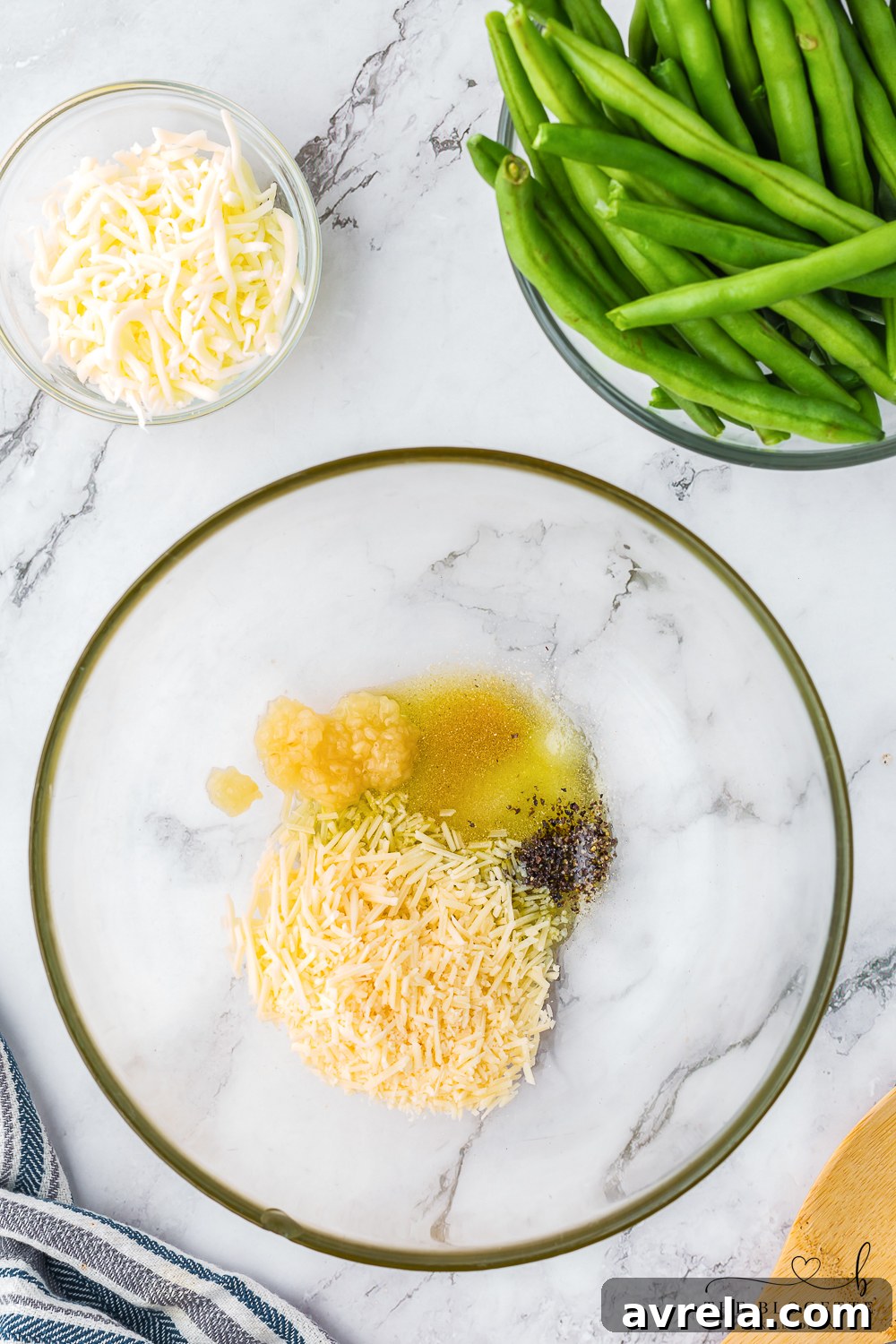 Close-up of green beans in a mixing bowl, coated with olive oil, onion powder, minced garlic, salt, pepper, and parmesan cheese, showing the seasoning process.