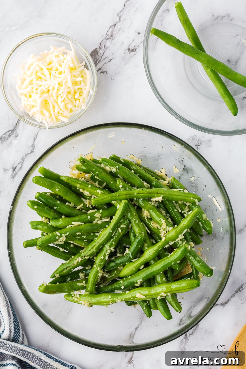 A close-up of fresh green beans in a large mixing bowl, tossed with a flavorful blend of olive oil, minced garlic, onion powder, and spices, ready for baking.