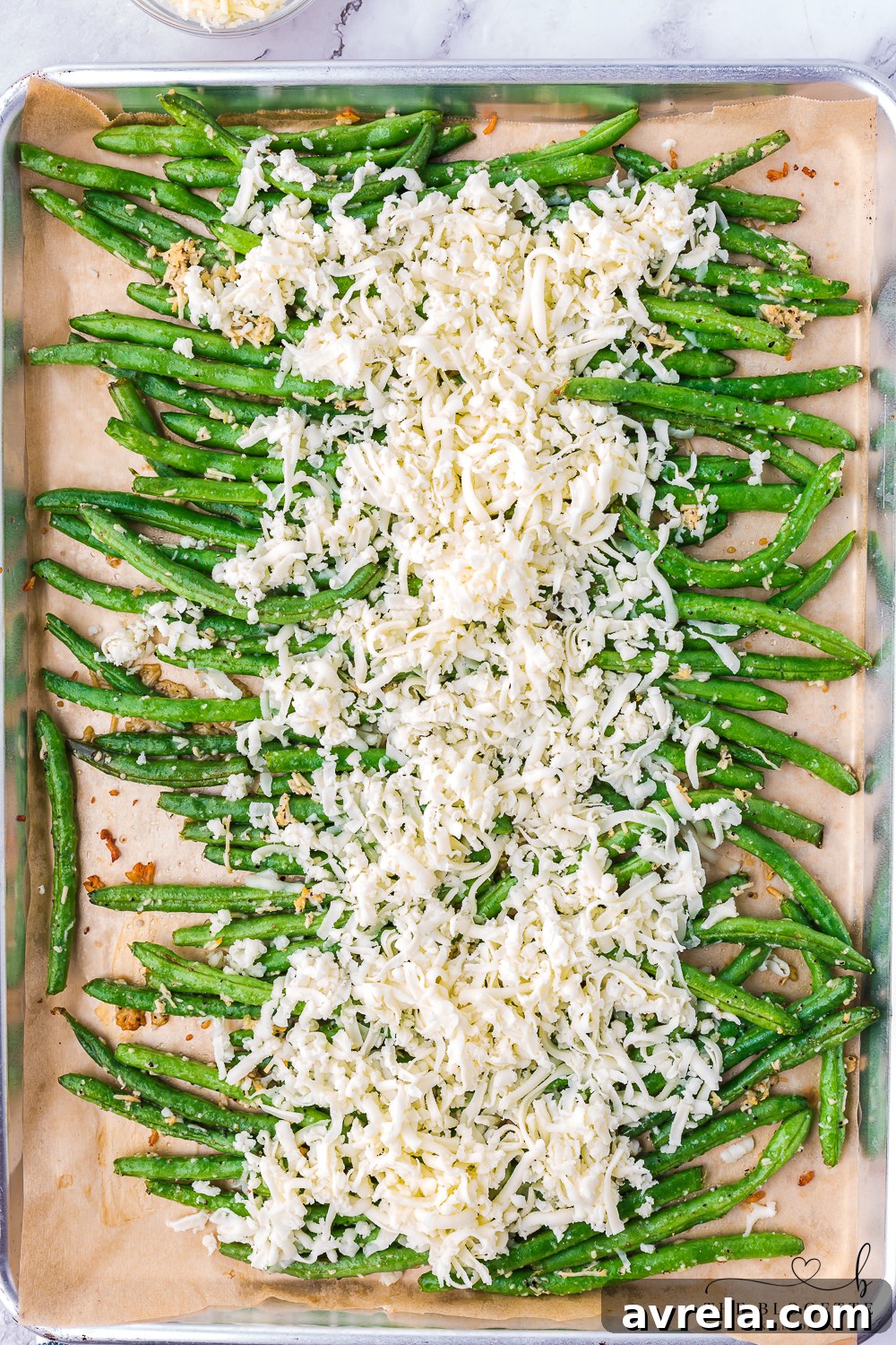 Melted mozzarella cheese generously sprinkled over hot, baked green beans on a baking sheet, ready for a quick broil to achieve golden perfection.