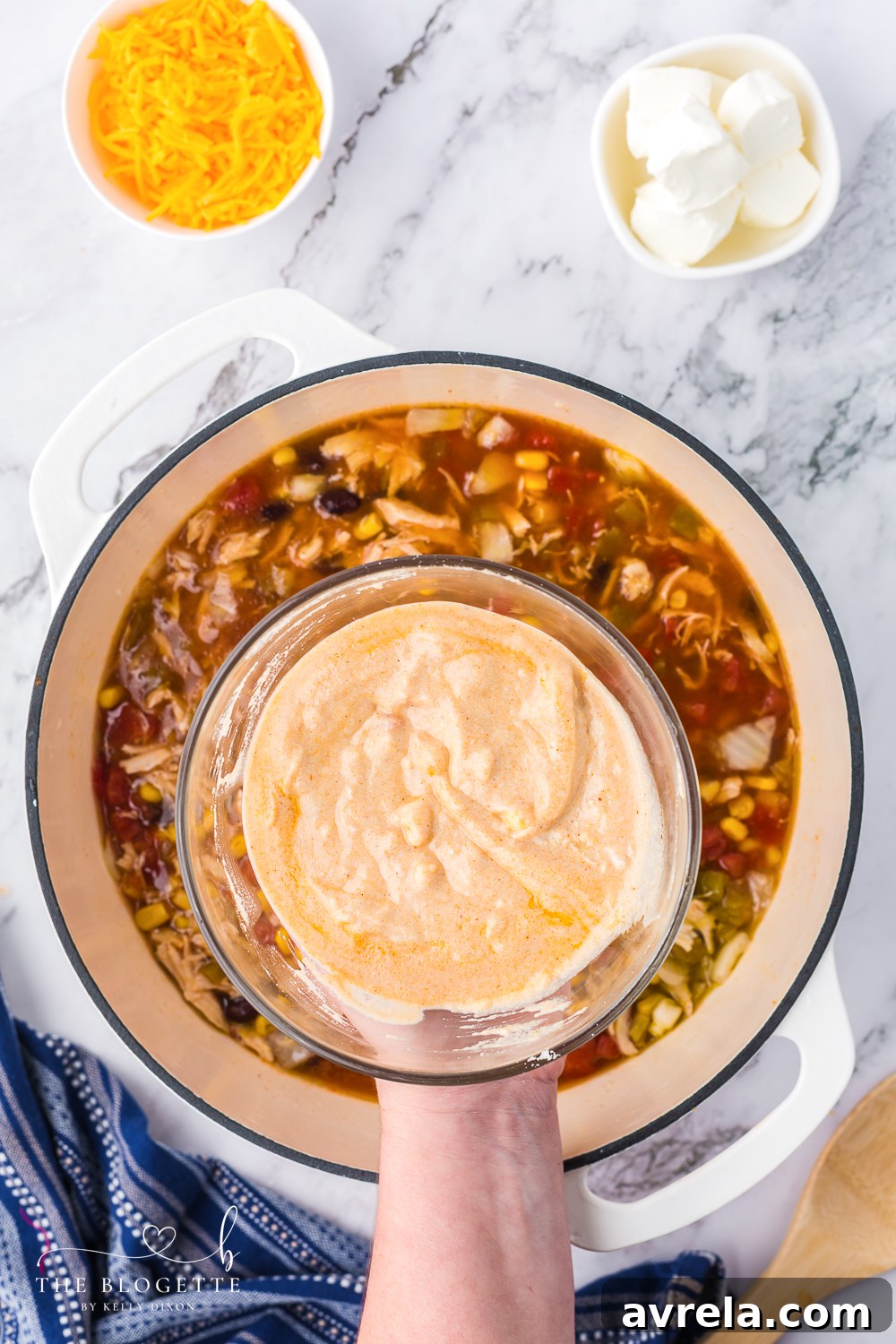 Adding shredded cheddar and cream cheese to the simmering chicken enchilada soup for a rich and creamy finish.