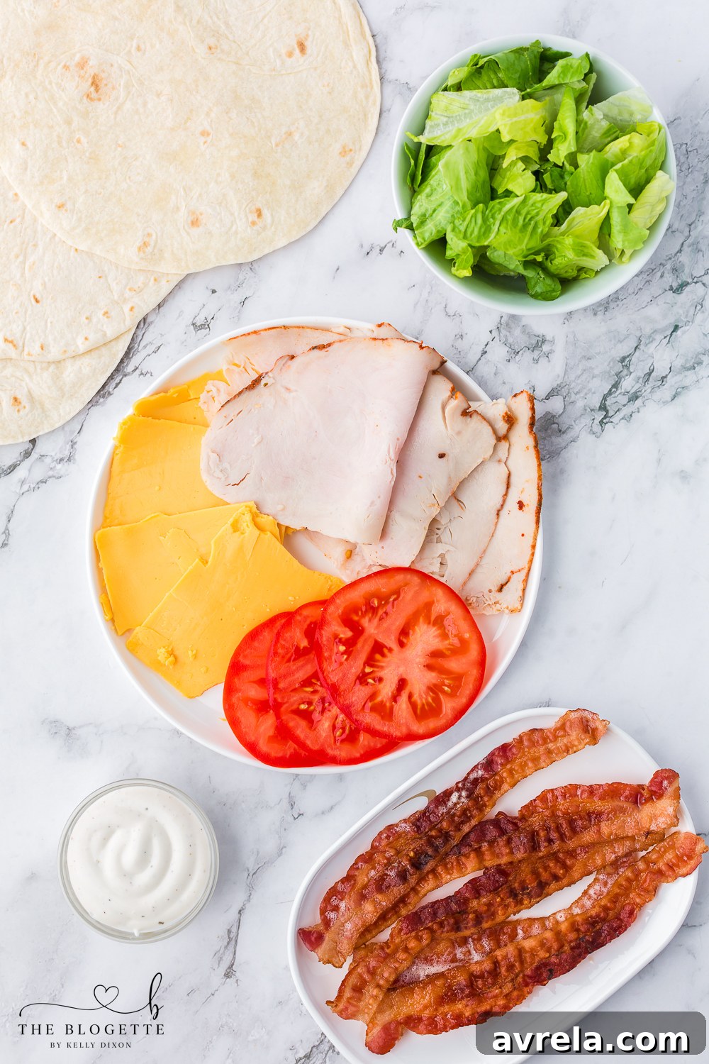 A selection of fresh ingredients laid out for a Turkey Ranch Club Wrap, including crisp romaine lettuce, vibrant tomato slices, and rich cheddar cheese, ready for assembly.