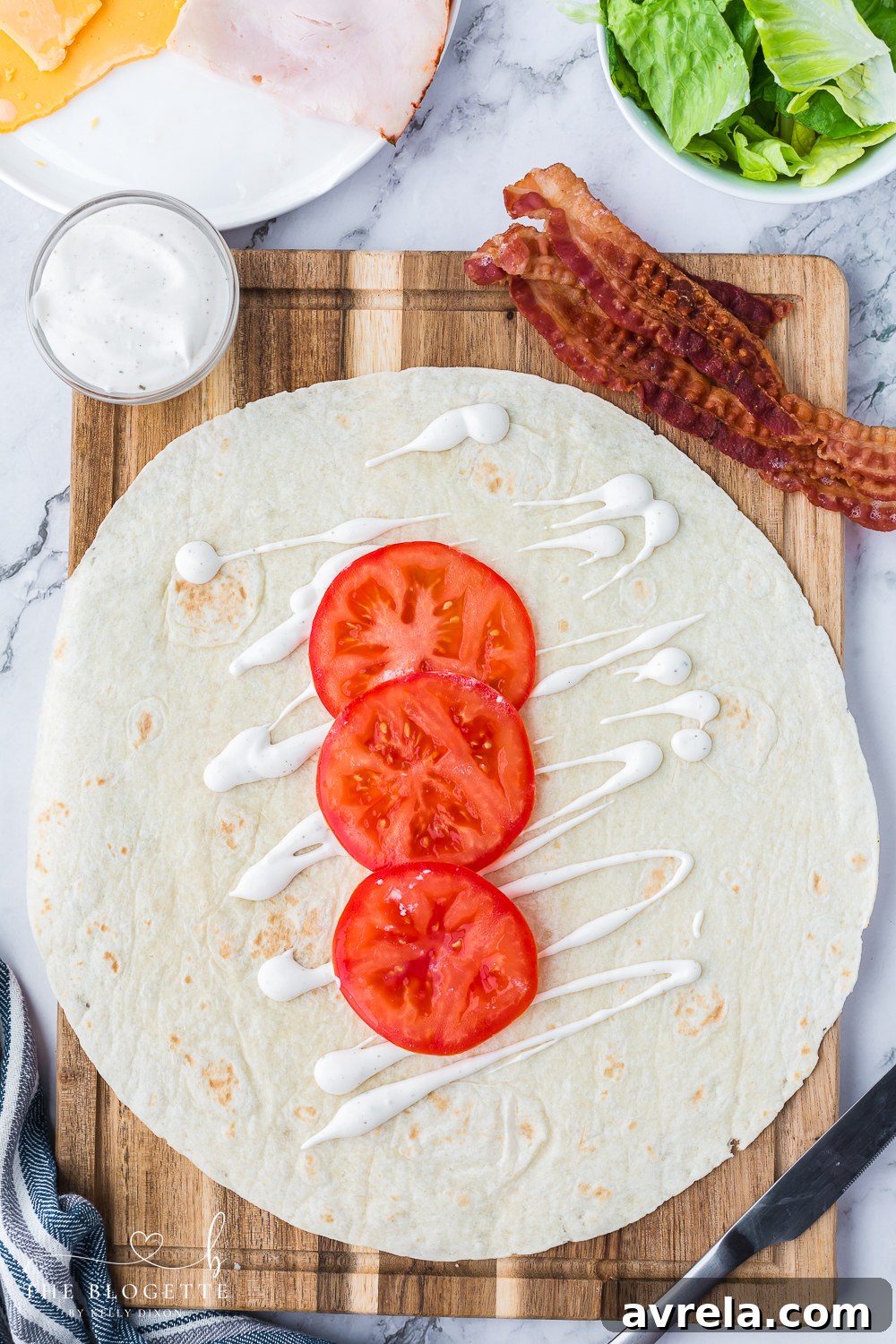 Close-up of fresh tomato slices next to a dollop of creamy ranch dressing on a cutting board, ready for the Turkey Ranch Club Wrap.