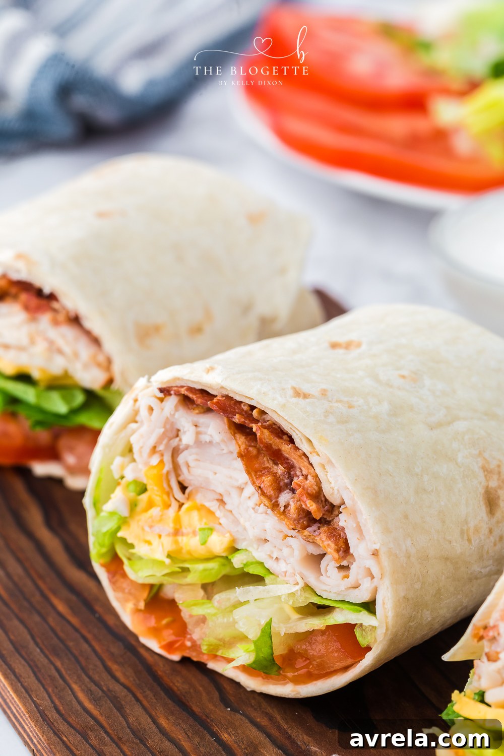 The ultimate Turkey Ranch Club Wrap, sliced in half to reveal layers of turkey, bacon, cheddar, tomato, and lettuce, drizzled with ranch dressing – perfect for lunch or dinner.