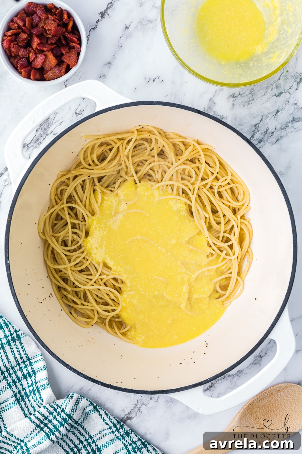 Adding the tempered egg and cheese mixture to hot spaghetti in a skillet, demonstrating the crucial step of rapidly tossing to create a creamy Carbonara sauce without scrambling the eggs.