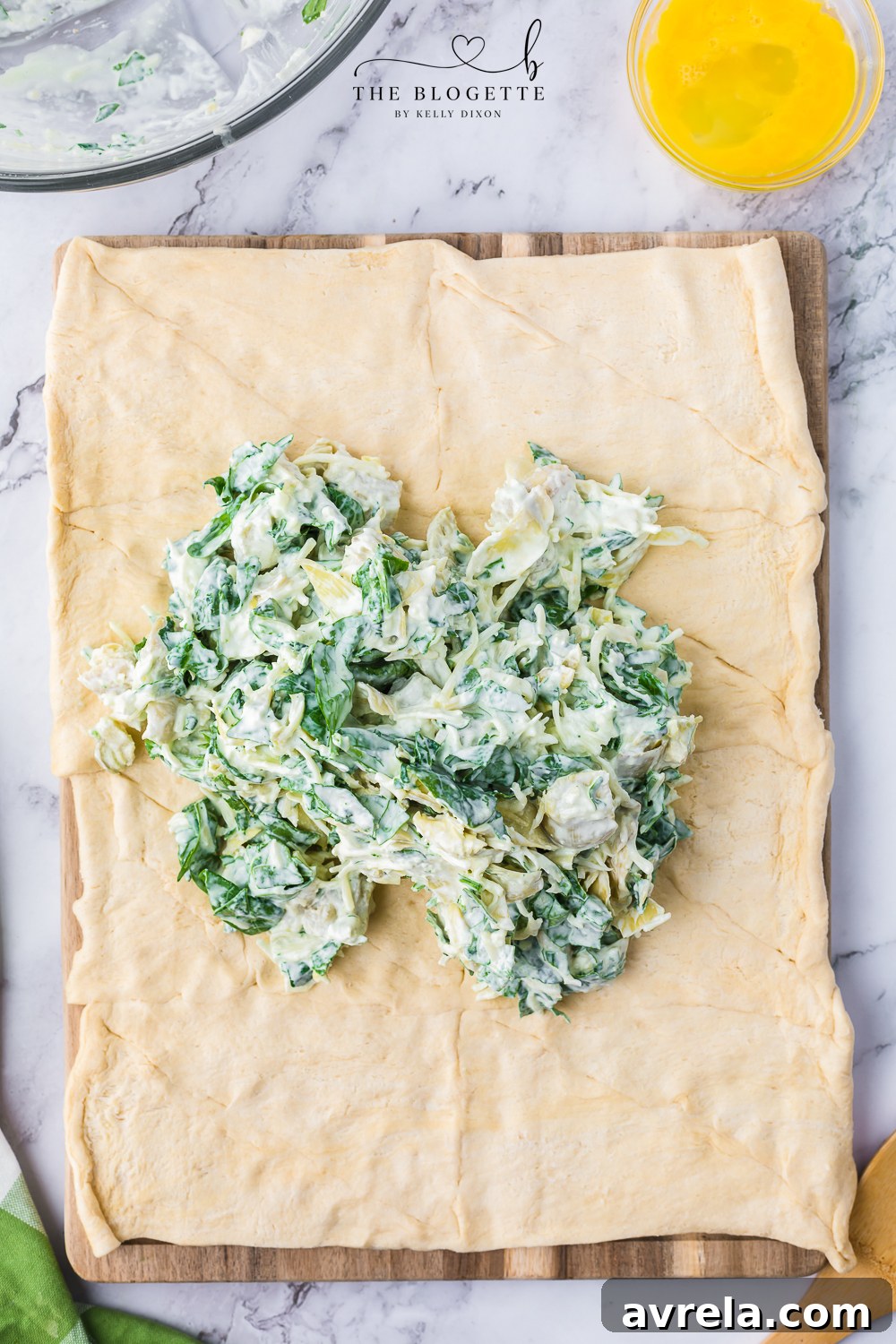 The creamy artichoke and spinach mixture being placed onto the flat crescent dough sheet, ready for spreading.