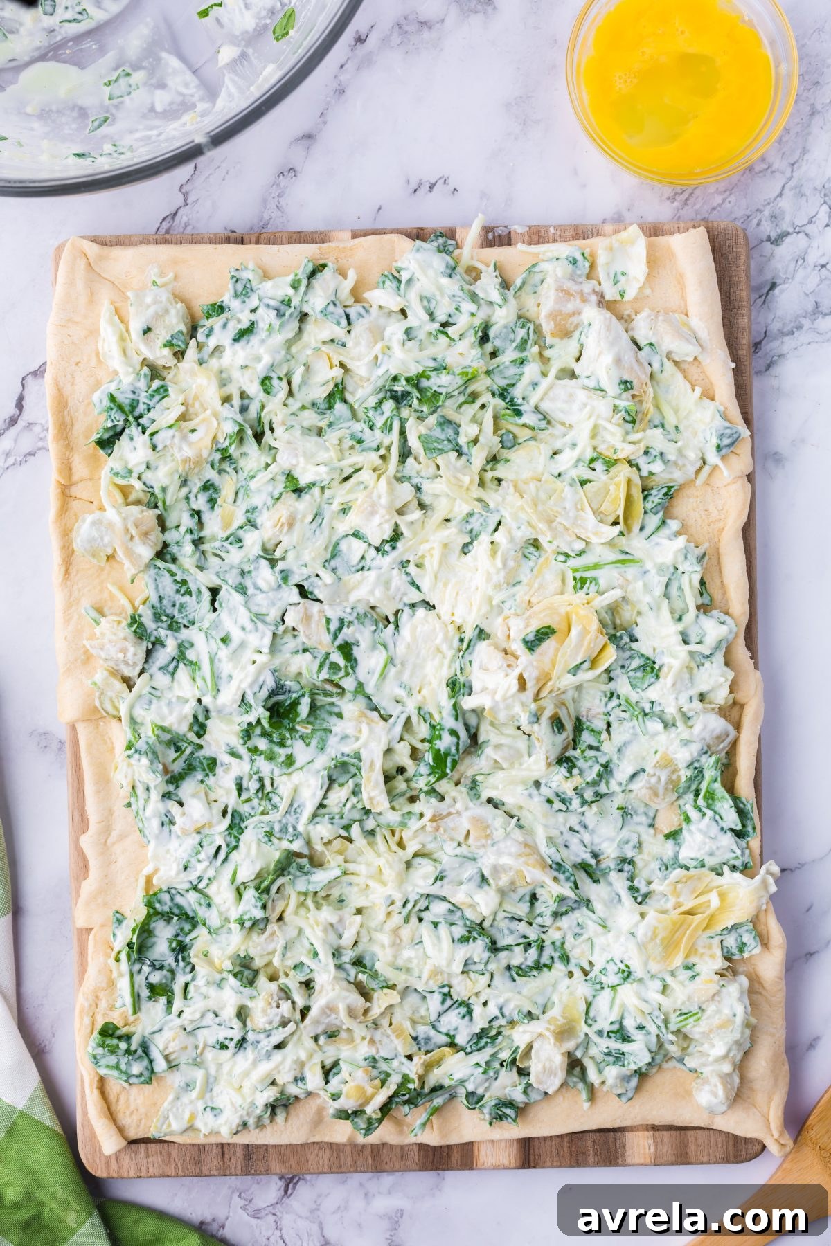 Spreading the savory spinach artichoke mixture evenly over the entire surface of the crescent roll sheet, preparing for rolling.