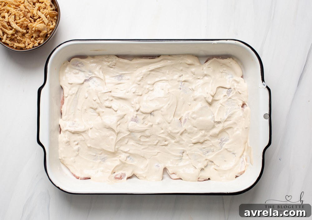 Creamy French onion sauce being spread over raw pork chops in a baking dish.