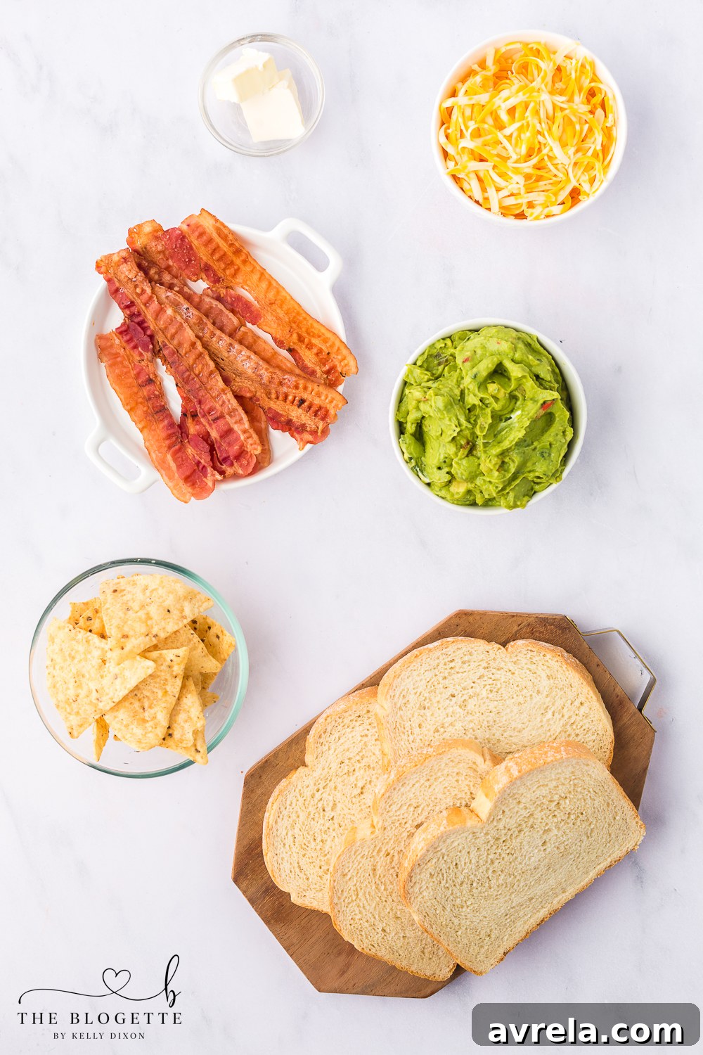 Ingredients laid out for Bacon Guacamole Grilled Cheese, including sourdough bread, butter, cheese, guacamole, bacon, and tortilla chips.