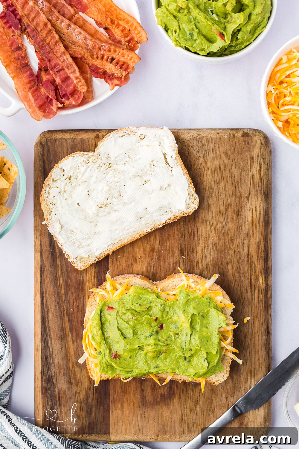 Spreading creamy guacamole and sprinkling cheese on a slice of sourdough bread for a grilled cheese sandwich.