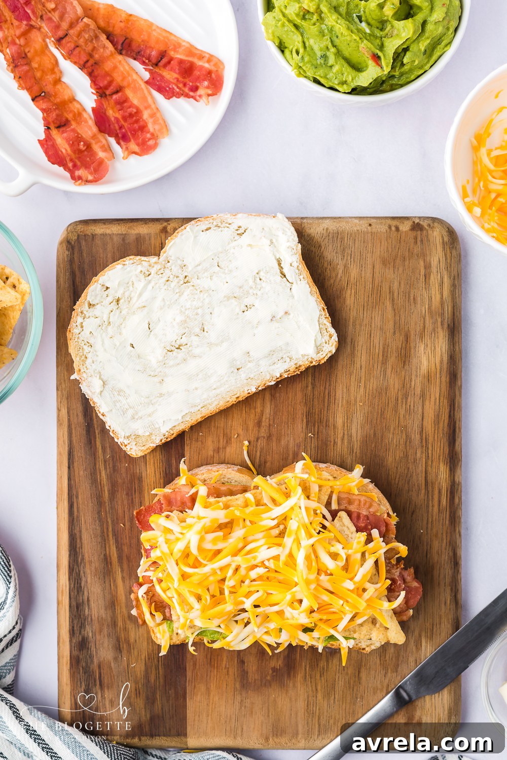 Topping the grilled cheese sandwich layers with more shredded cheese before the final bread slice.